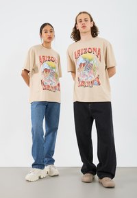 Beige cotton t-shirts with a colorful Arizona graphic, paired with blue and black jeans, and light-colored sneakers.
