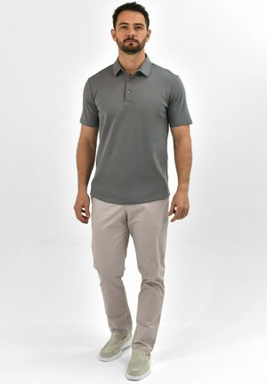 Grijze polo met korte mouwen, twee-knopen placket, geborduurd logo. In combinatie met lichtbeige broeken en grijze instapschoenen.