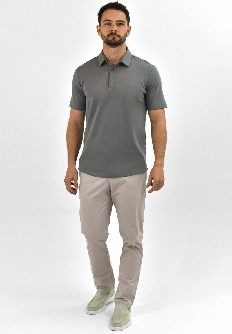Grijze polo met korte mouwen, twee-knopen placket, geborduurd logo. In combinatie met lichtbeige broeken en grijze instapschoenen.