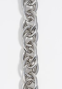 Cadena de metal plateado compuesta de eslabones ovalados entrelazados con un acabado pulido y una ligera curvatura, reflejando la luz con una textura suave.