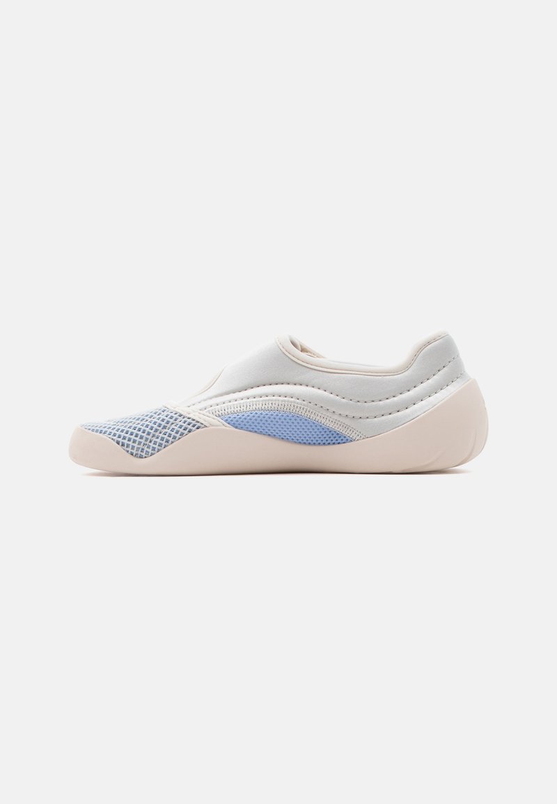 Scarpa slip-on bianca e azzurro chiaro con pannelli in mesh, suola morbida e cuciture minime, mostrata di profilo su uno sfondo neutro.