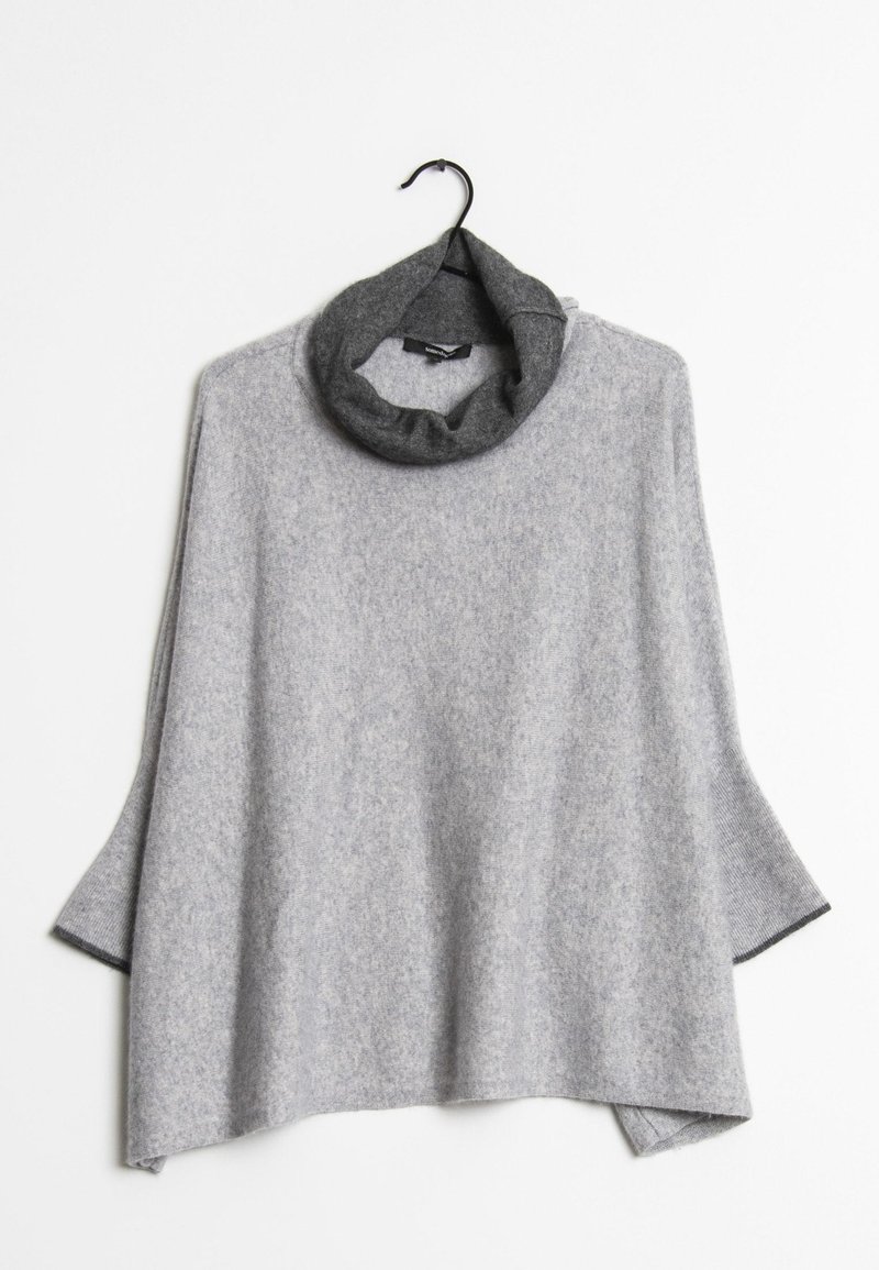Poncho en laine gris clair avec des manches larges et un col cheminée gris foncé, suspendu sur un cintre noir contre un fond blanc.