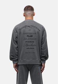 Felpa grigia dal fit rilassato, con grande testo stampato sulla schiena in vari caratteri e posizioni, che enfatizza diversi nomi di città.