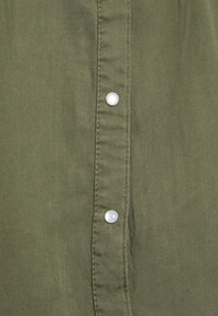 Close-up of olive green fabric with vertical seam and two white snap buttons fastened on a garment.