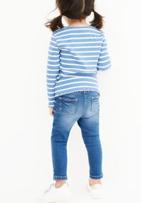 Modrá a biela pruhovaná blúzka s dlhým rukávom a vlnitým lemom, v kombinácii s džínsy úzkeho strihu v strednej umývanej farbe a bielymi teniskami s kovovými akcentmi.
