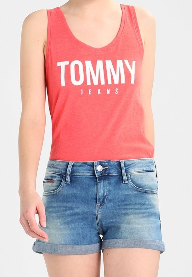Röd ärmlös topp med "TOMMY JEANS"-logotyp i vitt, i kombination med blå denimshorts med upprullade manschetter och femfickorsdesign.