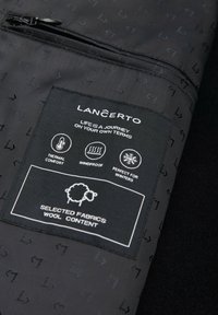 Czarna etykieta z materiału z instrukcjami pielęgnacji, logo "Lancerto" oraz ikonami symbolizującymi komfort cieplny, wiatroszczelność i zawartość wełny. Teksturowane tło.