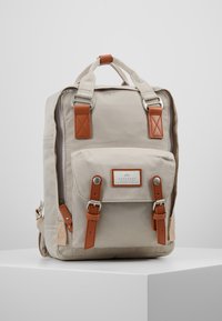 Sac à dos en toile beige avec des accents en cuir marron, de forme rectangulaire, poche à rabat à l'avant et bretelles réglables. Comprend du matériel en métal et des détails de couture.