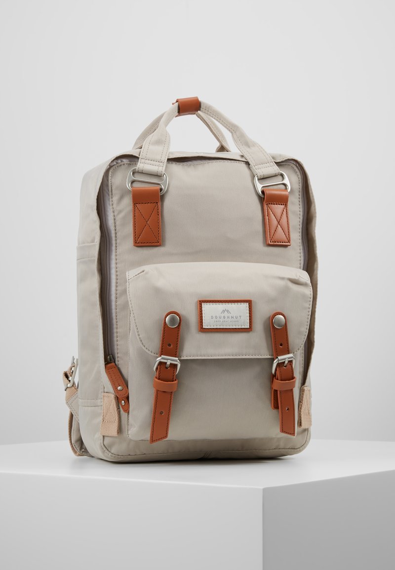 Sac à dos en toile beige avec des accents en cuir marron, de forme rectangulaire, poche à rabat à l'avant et bretelles réglables. Comprend du matériel en métal et des détails de couture.