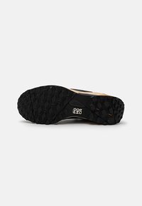 Svart gummisåle til sneakers med en teksturert, robust overflate; har sekskantede mønstre for godt grep; logo er til stede i designet.