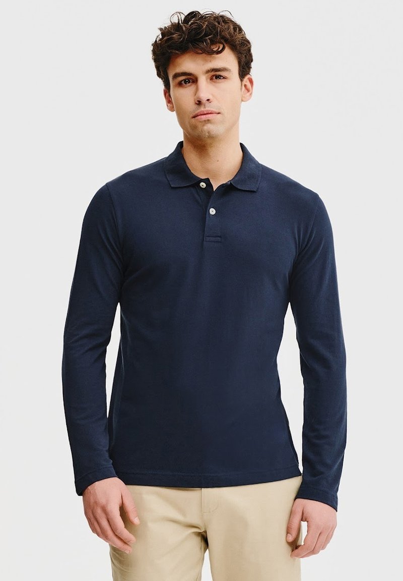 Granatowa koszula polo z długim rękawem, klasycznym kołnierzykiem, zapięciem na trzy guziki oraz miękką teksturą bawełny, zestawiona z beżowymi spodniami.
