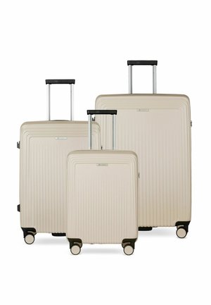 Trois valises rigides beiges de tailles variées avec poignées extensibles et quatre roues chacune, disposées côte à côte sur un fond blanc.
