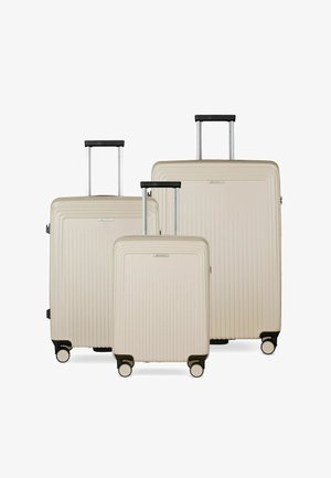 Trois valises rigides beiges de tailles variées avec poignées extensibles et quatre roues chacune, disposées côte à côte sur un fond blanc.