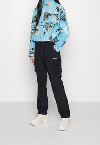 Blå blommönstrad tröjjacka med hög krage, kombinerad med svarta cargobyxor med sidofickor och orange detaljer. Vita chunky sneakers.