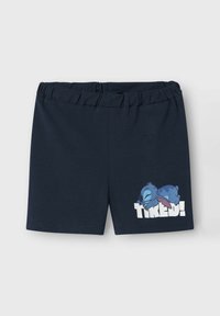 Donkerblauwe korte broek met elastische tailleband, met een slapende blauwe cartoonfiguur en het woord "MOE!" gedrukt op het rechterbeen.