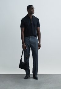 Polo negru cu mâneci scurte și fermoar, pantaloni gri croiți, și geantă neagră matlasată, completate de pantofi negri eleganți.