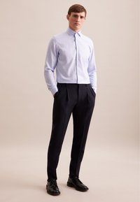Jasnoniebieska koszula w kratę z pointed collar, zestawiona z ciemnymi, dopasowanymi spodniami. Czarne, sznurowane buty. Gładkie tekstury tkanin.