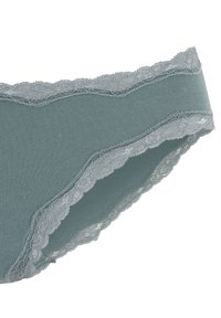 Kokvilnas maisījuma apakšveļa mierīgā teal krāsā ar sarežģītu mežģīņu apdari ap jostas un kāju atverēm, ar gludu tekstūru un elastīgu piegulšanu.