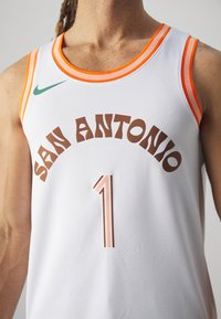 Camiseta de baloncesto blanca con ribetes naranjas, con "SAN ANTONIO" en texto marrón y el número "1" en un diseño texturizado con contorno. Incluye el logotipo de Nike.