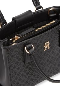 Μαύρη δερμάτινη τσάντα χειρός με ανάγλυφο σχέδιο, χρυστό φερμουάρ, χρυσό λογότυπο και στρογγυλεμένες λαβές συνδεδεμένες με χρυσούς κρίκους.