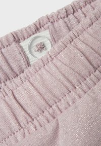 Tela de color rosa claro con un ligero brillo. Presenta una cinturilla elástica con textura fruncida y un detalle de botón blanco en el centro.