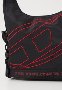 Sac en nylon noir avec des motifs et du texte brodés rouges "POUR RÉUSSIR." Dispose de bretelles ajustables et d'une texture lisse.