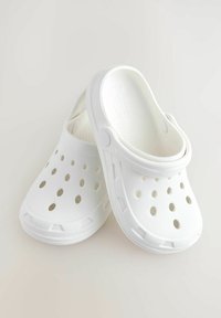 Weisse Clogs aus leichtem Kunststoff, mit durchlässigen Löchern für Atmungsaktivität, einer abgerundeten Zehenpartie und einem erhöhten Fersenbereich für Stabilität.