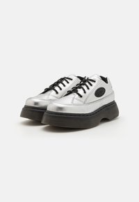 Srebrne sneakersy na platformie z czarnymi sznurowadłami, z zaokrąglonym czubkiem, gładkim metalicznym wykończeniem i teksturowaną czarną gumową podeszwą.
