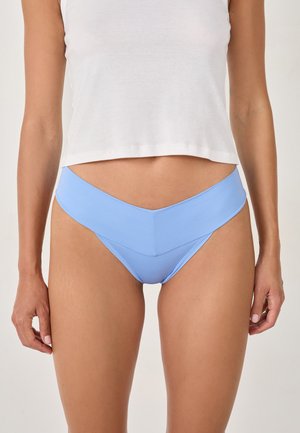 Mutandine azzurro chiaro con una texture liscia e una vita a forma di V, abbinate a un top corto bianco che mostra la pancia.
