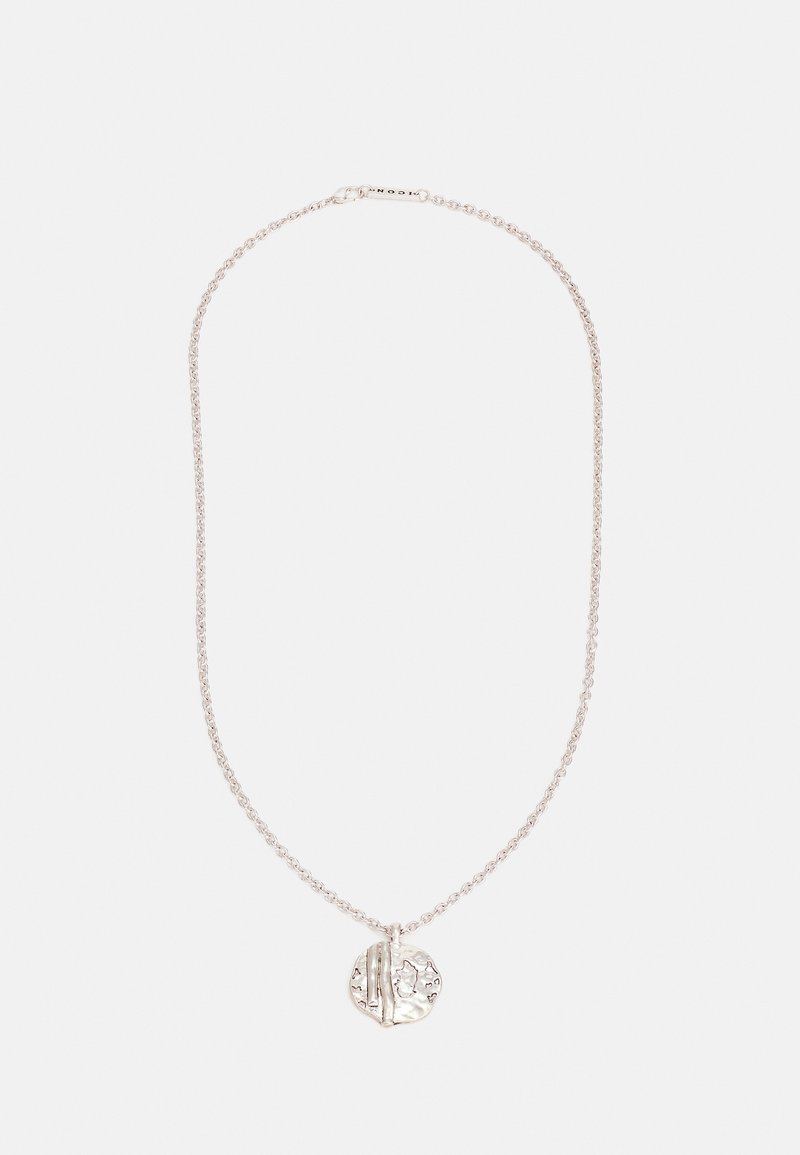 Colar de corrente prateada com um pendente redondo e texturizado, apresentando detalhes gravados. A corrente é delicada e entrelaçada.