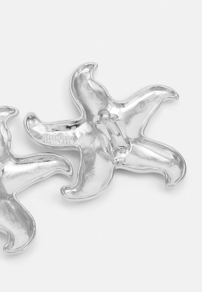 Clip per capelli a forma di stella marina in metallo argentato, con una superficie lucida e strutturata e una chiusura centrale. Presenta punte arrotondate e un design ondulato.