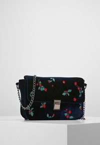 Tmavě modrá sametová kabelka s květinovou výšivkou v červené a zelené barvě, stříbrnými kovovými doplňky a kovovým řetízkem, vybavená magnetickým zapínáním.