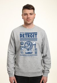 Felpa grigia con un design grafico retro. Il design include un personaggio di basket sorridente e la scritta "DETROIT" in bold blu.