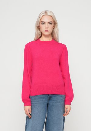 Pull en maille fuchsia avec des manches longues, des poignets et un ourlet côtelés, doté de délicates épaules bouffantes. Associé à un jean bleu large.