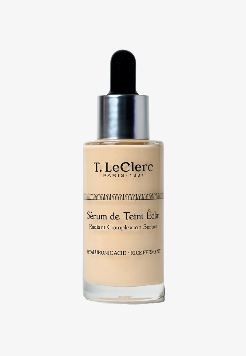 Beige glass serum bottle with a black dropper, labeled "Sérum de Teint Éclat," featuring text details and a decorative silver band.