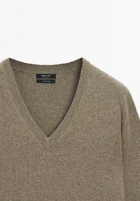 Pull en cachemire vert olive avec un col en V et un col côtelé. Présente un tissu doux et texturé ainsi qu'une étiquette indiquant la marque et le matériau.