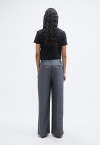 Γκρι παντελόνια με φαρδιά γραμμή, με εφαρμοστή σχεδίαση, δύο πίσω τσέπες με κουμπιά και λεία υφή υφάσματος. Συνδυασμένα με μαύρο t-shirt.