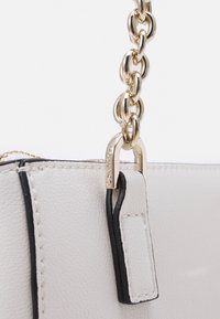 Borsa in pelle bianca testurizzata con un accento nero, tracolla in catena dorata e moschettone in oro stampato con "Calvin Klein."