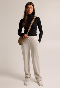 Black long-sleeve top paired with light gray sweatpants, featuring side pockets. A tan crossbody bag complements the outfit. White sneakers included.