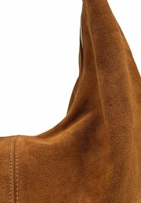 Sac en cuir suédé marron avec une texture douce et une forme courbée. Présente des coutures visibles et un détail de fermeture éclair sur le côté.