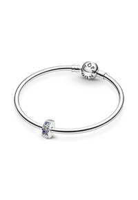Srebrna zapestnica s gladko trakico, ki vključuje teksturiran dodatek okrašen z modrimi dragulji in okroglo zaponko označeno z "Pandora."
