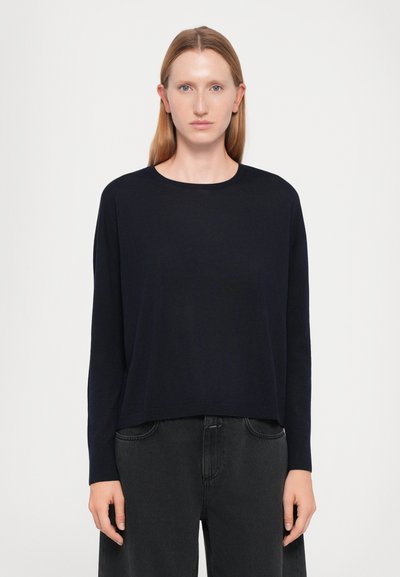 Donkerblauwe sweater met lange mouwen en ronde halslijn, ontspannen pasvorm, zachte textuur en recht aan de onderkant, gecombineerd met zwarte hoog getailleerde broek.