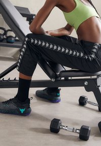 Pantaloni sportivi neri con strisce bianche del logo Kappa, abbinati a scarpe nere texture con accenti turchesi e suole viola. Crop top verde.