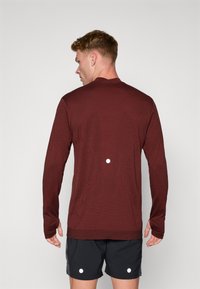 Bordo majica dugih rukava od teksturiranog materijala, s okruglim ovratnikom, uskim krojem i reflektirajućim detaljem na leđima.
