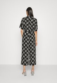 Combinaison à manches courtes noir et blanc à motifs, jambes larges et taille cintrée. Présente des dessins abstraits, portée avec des sandales à talons hauts.