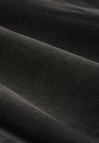 Czarna tkanina prezentuje miękką, teksturowaną powierzchnię z wyraźnymi fałdami, wykazując subtelny połysk i jednolity wzór splotu.