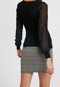 Black top with sheer long sleeves, paired with a fitted plaid mini skirt in black, white, and gold hues. Smooth fabric with a structured fit.