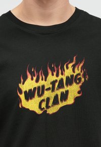Μαύρα μπλουζάκια με ένα τολμηρό γραφικό σχέδιο φλόγας σε κίτρινο και κόκκινο, με το κείμενο "WU-TANG CLAN" σε στυλιζαρισμένη γραμματοσειρά.