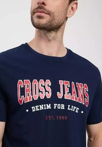 Granatowa bawełniana koszulka z odważnym, białym i czerwonym napisem "CROSS JEANS", z mniejszym napisem "DENIM FOR LIFE" oraz "EST. 1990" poniżej.