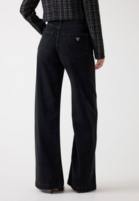 Sz�éles szárú fekete denim nadrág magas derékkal, két hátizsebbel, amelyeken háromszög alakú logó található, valamint letisztultan finishelve az alján.
